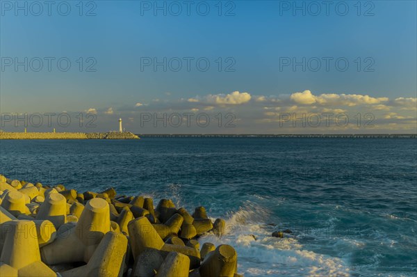 Calm seascape of coastline with tetrapods and lighthouse under a dusky blue sky, in South Korea