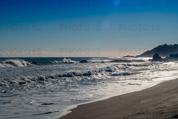 Rugged seascape with waves under bright morning sun crash onto beach and rocks under a beautiful blue sky, in South Korea