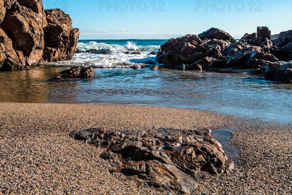A serene beach scene with waves crashing against large rocks under a clear blue sky, in South Korea