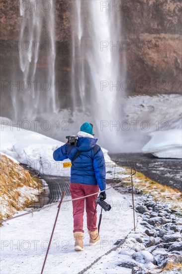 Female photographer from behind in winter in Iceland visiting the Seljalandsfoss waterfall