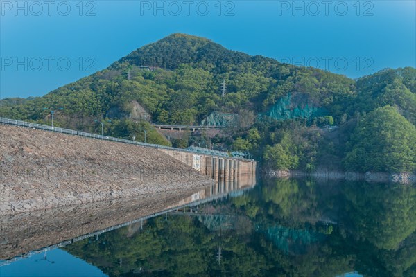 Beautiful lake area with dam and treeline reflected off the calm blue water at Daecheon Lake in South Korea