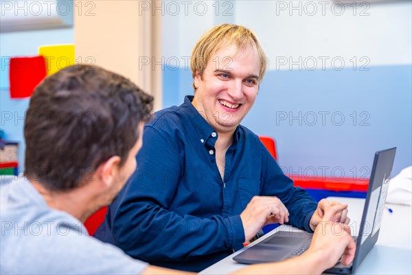 Happy mental disabled man and teacher in IT class in a day center for people with special needs
