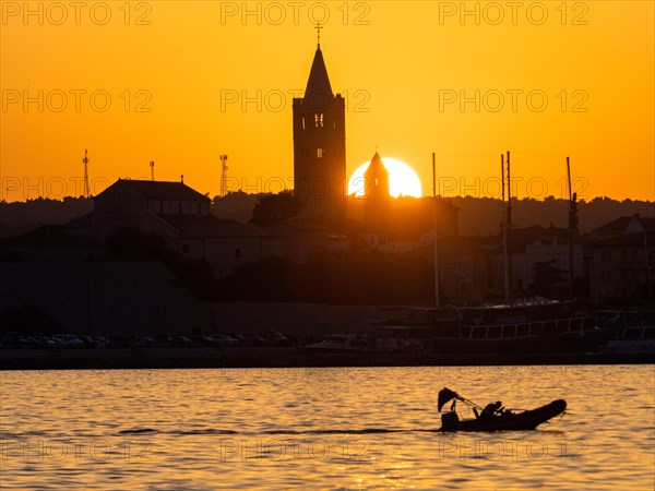 Motorboat in the golden evening light at sunset, silhouette of the church towers of Rab, town of Rab, island of Rab, Kvarner Gulf Bay, Croatia, Europe
