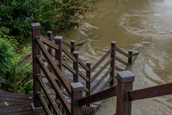 Wooden staircase leading to boardwalk submerged in river after torrential monsoon rains in Daejeon South Korea