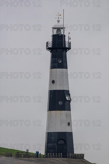A black and white lighthouse, shrouded in fog, rises up on a calm coastline