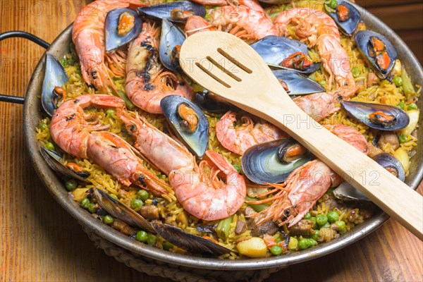 A paella full of seafood, peas, and rice served in a pan with a wooden spoon, typical Spanish cuisine, Majorca, Balearic Islands, Spain, Europe