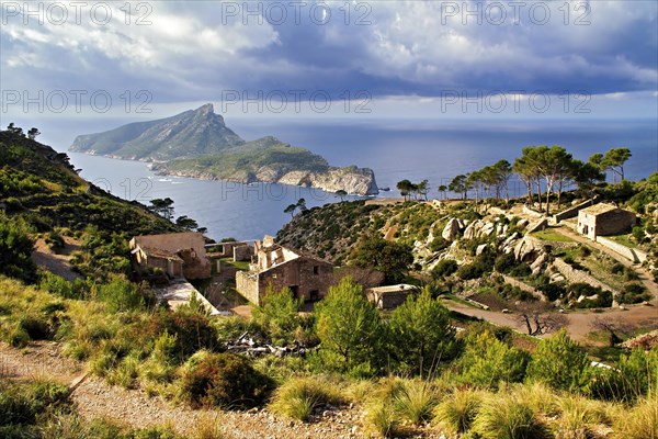 Ruins of a historic village perched on a cliff above the sea under a dramatic cloudy sky, Hiking tour in Tramuntana Mountains, Mallorca