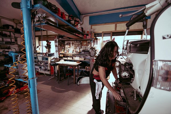 View of a hispanic young long haired brunette female mechanic working diligently in a packed workshop on a scooter, latino woman in traditional masculine jobs concept, feminine power in real life