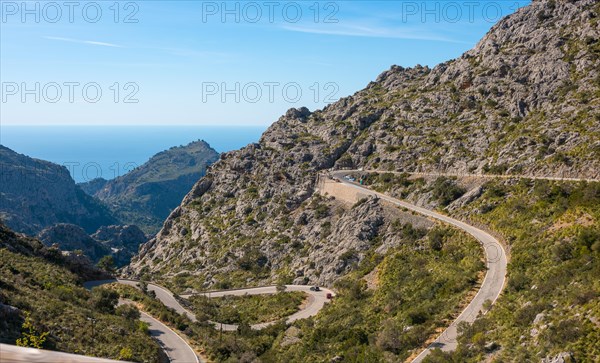 Mountain landscape with winding mountain road from Sa Calobra to Torrent de Pareis, cars and a cyclist on serpentines with various hairpin bends, hairpin bends, hairpin bends, steep, partly bare rock faces and peaks, construction site after collapse of a retaining wall, Mediterranean vegetation, Serra de Tramuntana mountains, view of the blue Mediterranean Sea in sunny weather and blue sky, steep coast, panoramic road, Majorca, Spain, Europe