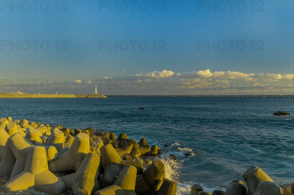 A lighthouse oversees the calm sea with tetrapods used for coastal protection at dusk, in South Korea