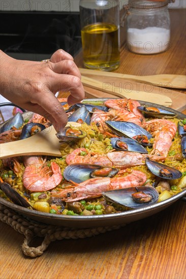 Hand gently stirring a seafood paella with shrimp and mussels using a wooden spatula, typical Spanish cuisine, Majorca, Balearic Islands, Spain, Europe