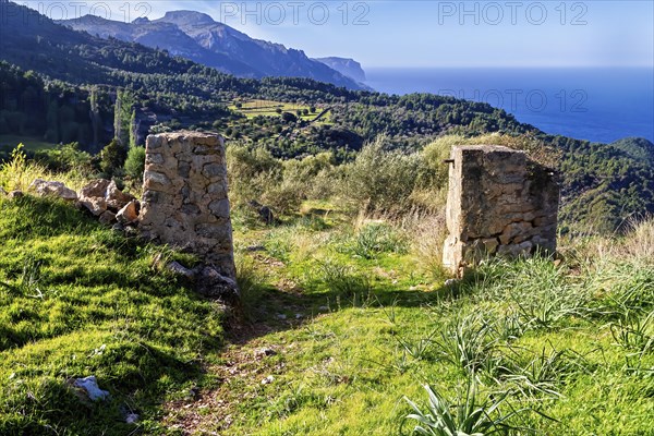 Stone pillars frame a rural scene with green fields and distant mountains, Hiking tour from Estellences to Banyalbufar, Mallorca