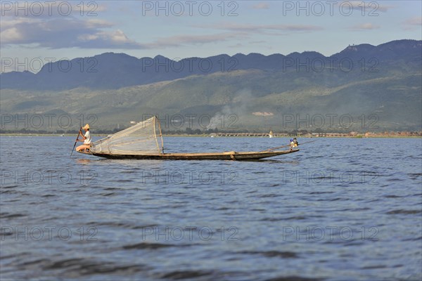 Fisherman in traditional boat working on a lake, mountains in the background, Inle Lake, Myanmar, Asia