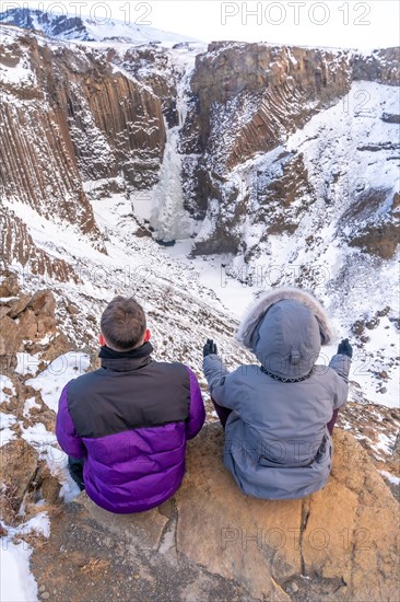 A couple meditating in winter in Iceland at the frozen Hengifoss waterfall