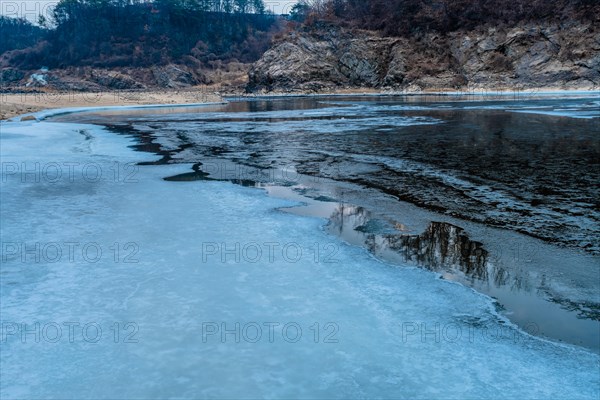 Close-up of cracked ice on a frozen river with forest in the background, in South Korea
