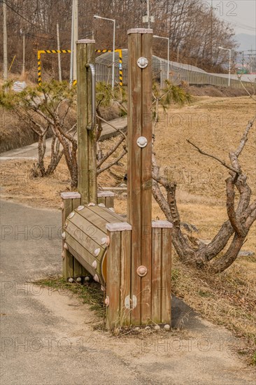 A quirky wooden seat structurally integrated with poles on a path by the grass, in South Korea