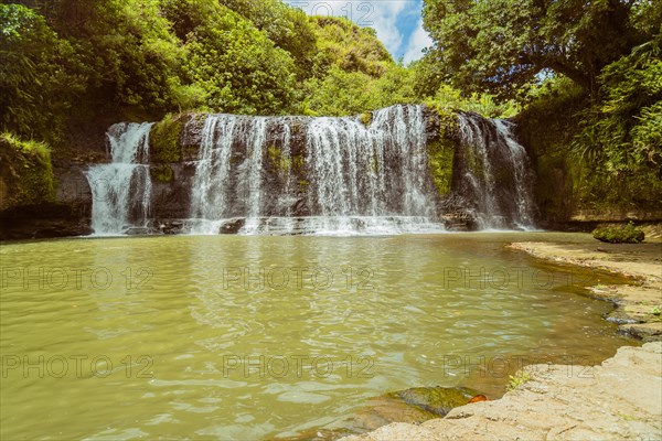Landscape of a waterfall with trees and blue sky in the background and water basin in the foreground in Guam