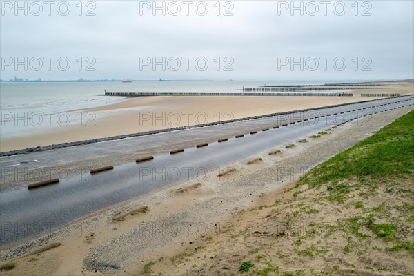 View of beach defence structures along a wet coastal road under cloudy skies, Breskens, Zeeland, Netherlands