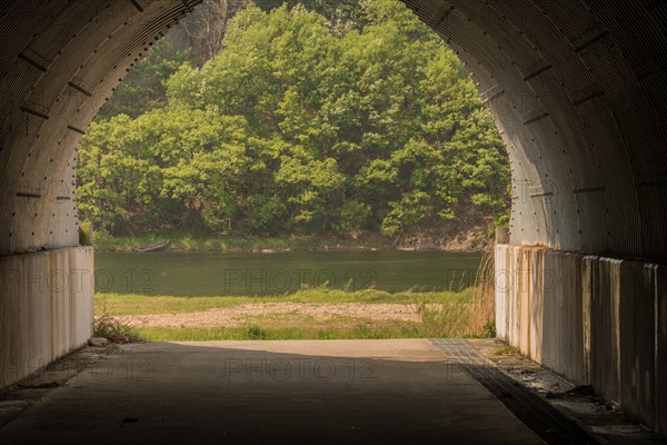 View of small boat on far tree lined river bank seen through a concrete underpass in South Korea