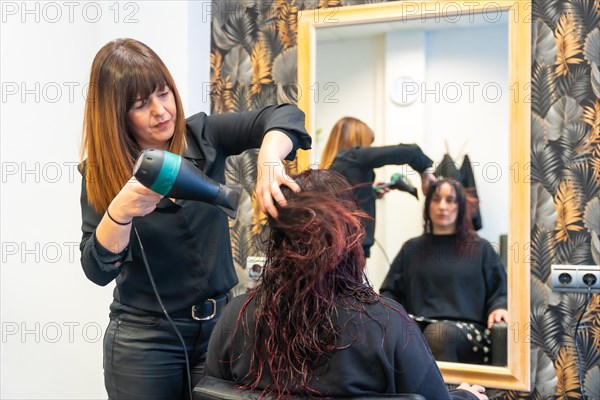 Hairstylist drying the hair of a woman in front of a mirror in the salon