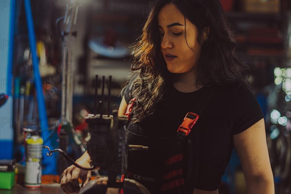Focused mechanic female repairing a scooter engine part in a workshop, a complete tool panel in background with bokeh effect, traditional male jobs by Mixed-race latino woman
