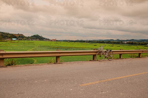 A lone bicycle leans against a guardrail on a country road overlooking lush green fields