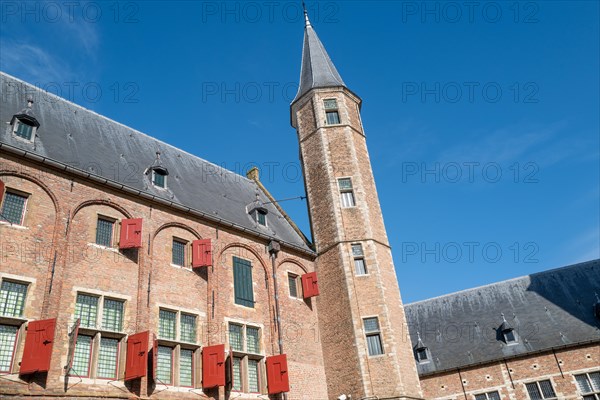 Old building with red shutters and tower-shaped extension under a clear blue sky