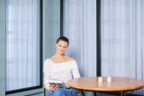 Carefree woman sits at a table in a cafe and thoughtfully looks at a book while waiting for her order