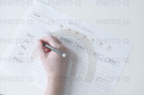 Diabetes log, daily log of food and insulin administration, food log, hand of a child holding a pen and appearing to fill in the log, the paper lies on a white table, Ruhr area, Germany, Europe