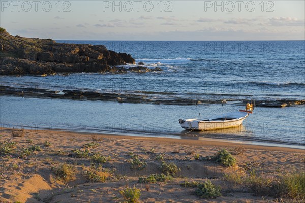 Tranquil scene of a single boat on the coastline with rocks in the soft evening light, Finikounda, Pylos-Nestor, Messinia, Peloponnese, Greece, Europe