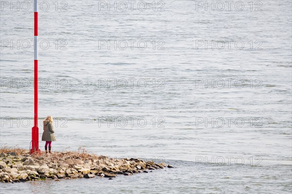 A person stands alone next to a lighthouse sign on the riverbank