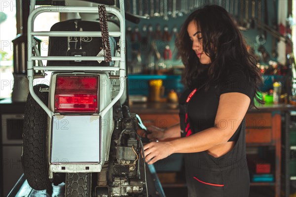 A hispanic young sensual female mechanic inspecting a rear car light in an automotive workshop, latino woman in traditional masculine jobs concept, feminine power in real life