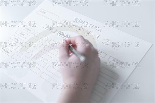 Diabetes log, daily log of food and insulin administration, food log, hand of a child holding a pen and appearing to fill in the log, the paper lies on a white table, Ruhr area, Germany, Europe