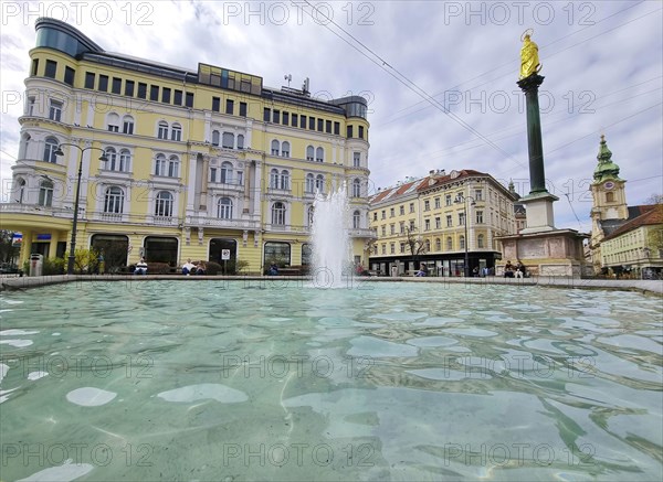 Graz, Austria, 26.03.2023: Mary's Column and fountain in Jakominiplatz Square and Parish Church in the background, famous attraction in the city center of Graz, Steiermark region, Austria, Europe