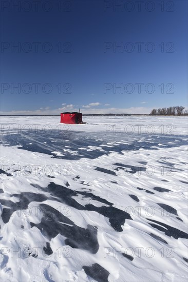 Winter, red fishing hut with snow drifts on a frozen riverscape, Saint Lawrence River, Province of Quebec, Canada, North America