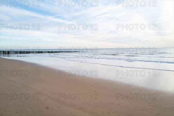 Empty beach overlooking a calm sea, damp sand reflects the sky