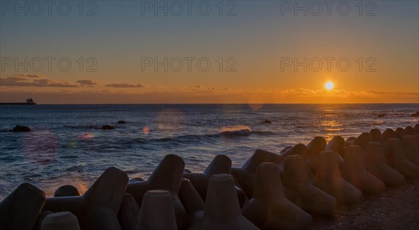 Tranquil sunset with orange sky over sea and tetrapods lined up on the coast, in South Korea