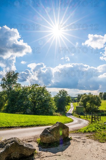 A rural scene with a path, rocks and bright sun in a partly cloudy sky, Wuelfrath, Mettmann, Bergisches Land, North Rhine-Westphalia