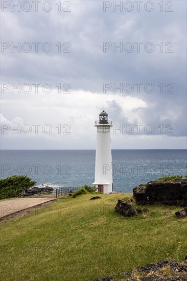 White lighthouse on a steep coast. Dramatic clouds with a view of the sea, pure Caribbean at Le Phare du Vieux-Fort, on Guadeloupe, French Antilles, France, Europe