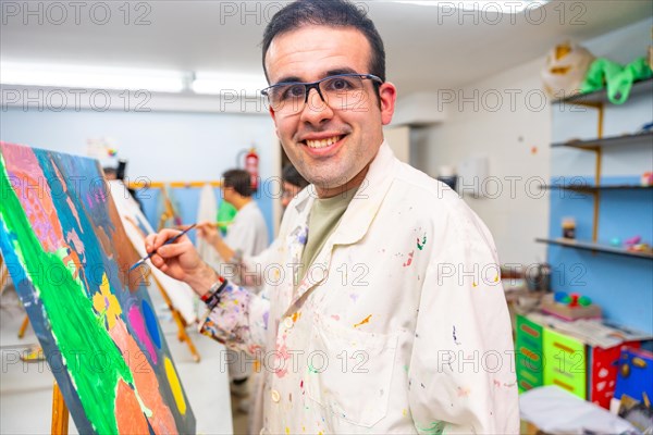 Disabled man looking at camera and smiling happy while painting on canvas