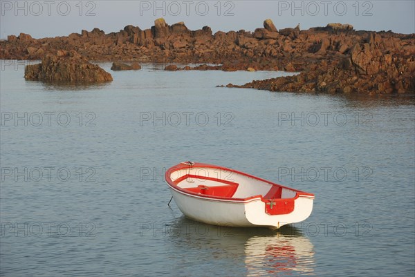 A lone red and white boat floating on calm sea water with rocks in the background