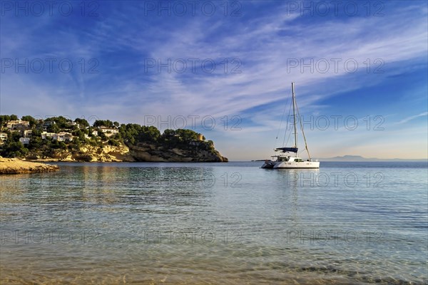 Yacht anchored near the beach with coastal homes under a sunset sky, Coastal Hiking tour in the south of Mallorca