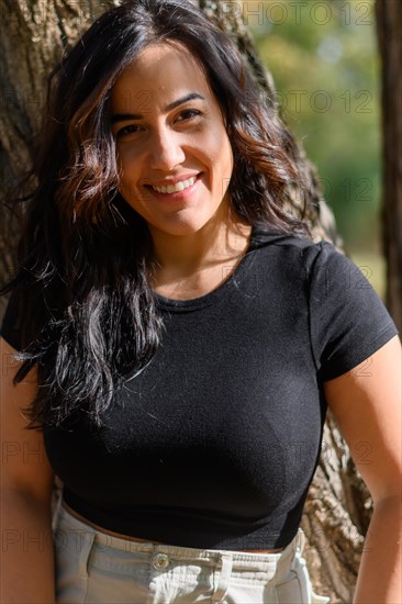 Joyful Cheerful hispanic young woman with a beaming smile in a black shirt outdoors, blurred background with bokeh, daytime, AI generated