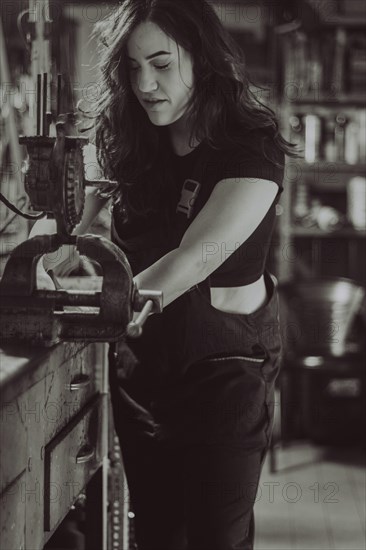 Craftswoman engaged in work using a vise on a bench in workshop, real women performing traditional man jobs of the past, black and white photograph