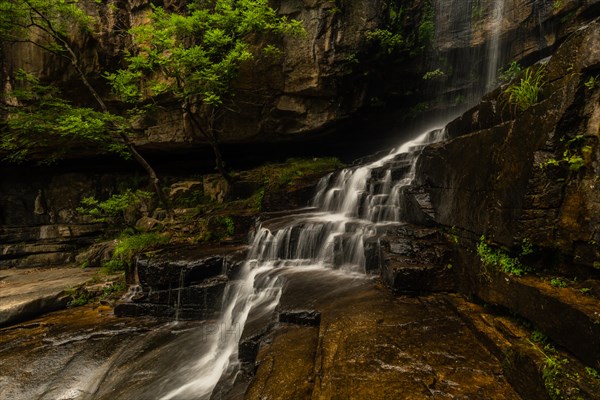 A tranquil waterfall flows over rocks and moss, resembling a fluid veil in nature, in South Korea