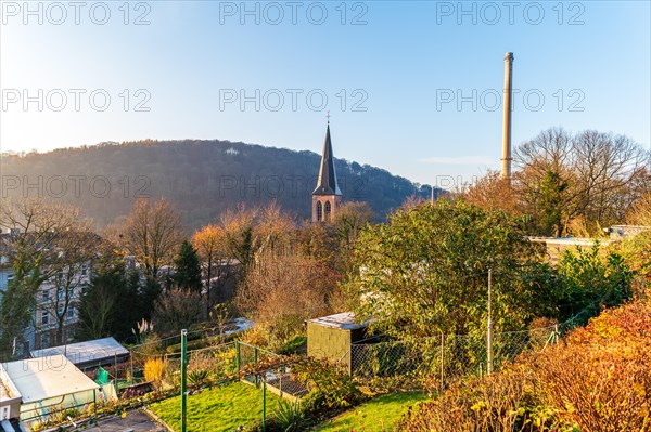 Sunrise over a town with a church tower, autumn trees and an industrial area in the background, Arrenberg, Elberfeld, Wuppertal, Bergisches Land, North Rhine-Westphalia