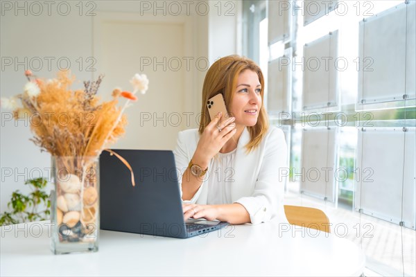 Female administrator talking to the phone while using laptop working in the office