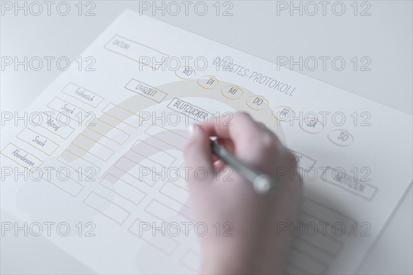 Diabetes log, daily log of food and insulin administration, food log, hand of a child holding a pen and appearing to fill in the log, the paper lies on a white table, Ruhr area, Germany, Europe