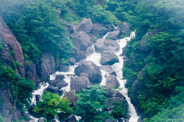 Misty waterfall cascades over large boulders in a lush green forest setting, in South Korea