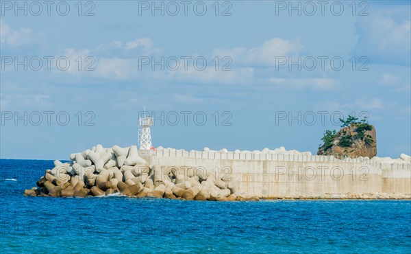 Sunlit maritime scene with lighthouse behind a sea defense wall, in South Korea